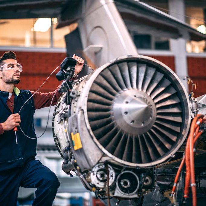 Aircraft mechanic probing an opened jet engine of an airplane with a portable camera and looking at the monitor in the maintenance hangar.